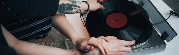 cropped view of tattooed couple putting vinyl record on record player