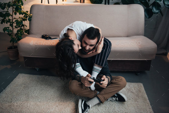 woman hugging and kissing man playing video game with joystick in living room