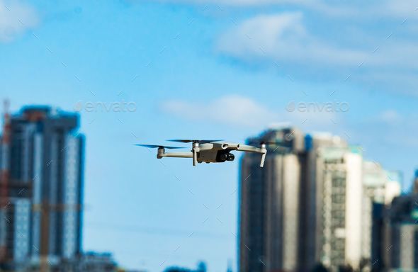 Beautiful shot of a quadcopter mini drone flying between blurred buildings with a blue sky