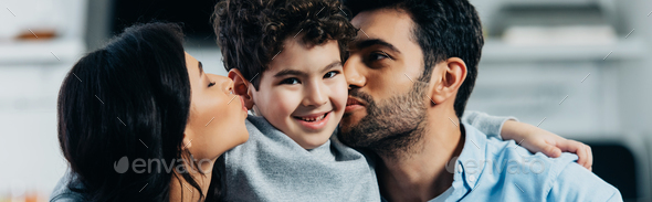 happy latin father and mother kissing cheeks of adorable son at home