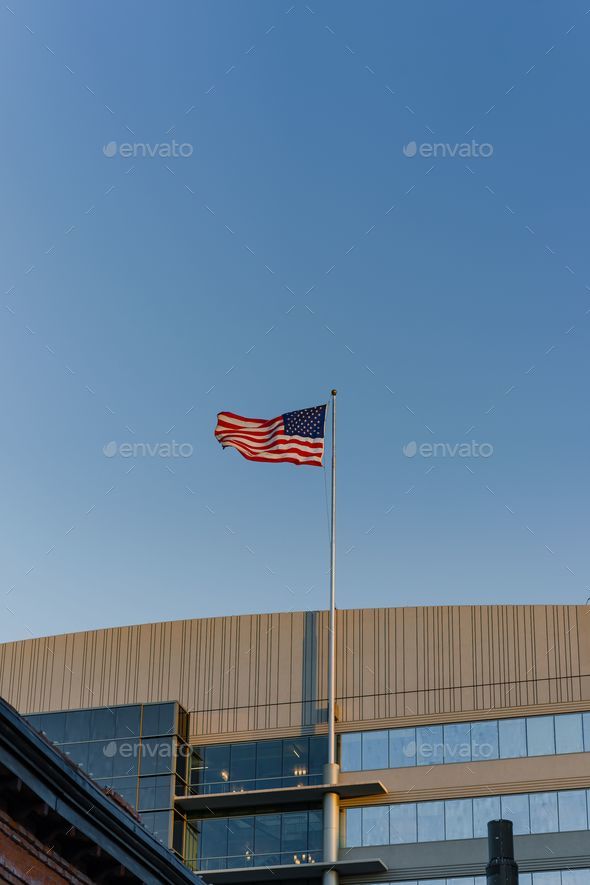 Vertical shot of an American flag waving against a blue sky outside a building