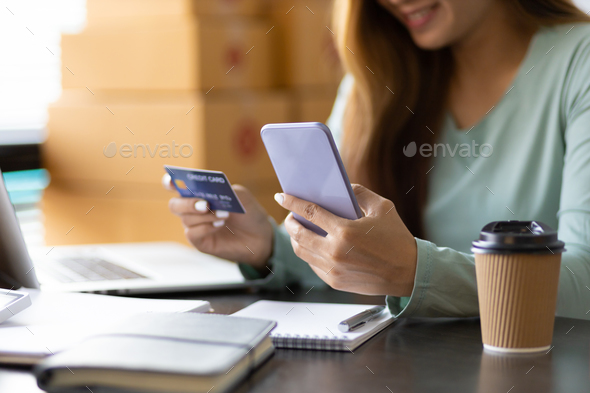 Woman holds a credit card and uses a mobile phone to check online balance and make online shopping.