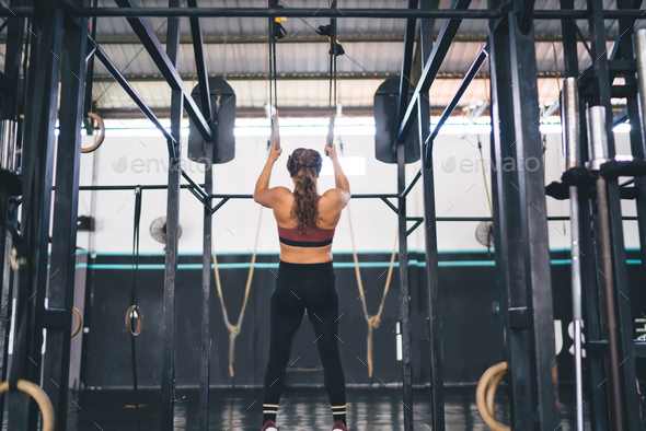 Fit woman doing pull ups with gymnastic rings at the gym or at