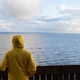 Man tourist in yellow raincoat watching sea on cold cloudy day looking at water, listening waves - PhotoDune Item for Sale