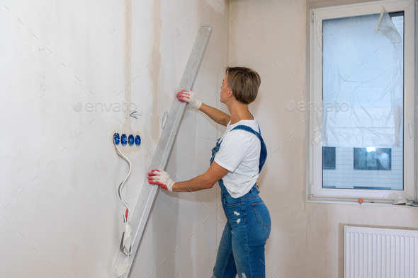 Renovation at home. Woman makes repairs in new apartment. Worker levels walls with building water