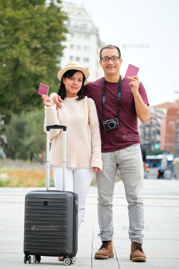 Happy multi-ethnic traveler couple holding passports and looking at camera.
