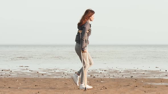 A woman on crutches walks along the beach, throws crutches and tries to walk without crutches alt