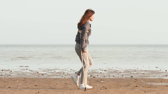 A woman on crutches walks along the beach, throws crutches and tries to walk without crutches
