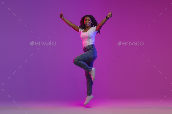 Happy Black Lady Jumping Up In Neon Light And Showing Thumbs Up