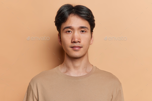 Portrait of serious dark haired adult Asian man with neutral facial expression focused at camera
