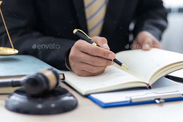Legal counsel is writing a note on a notepad while working in a lawyer\'s office.