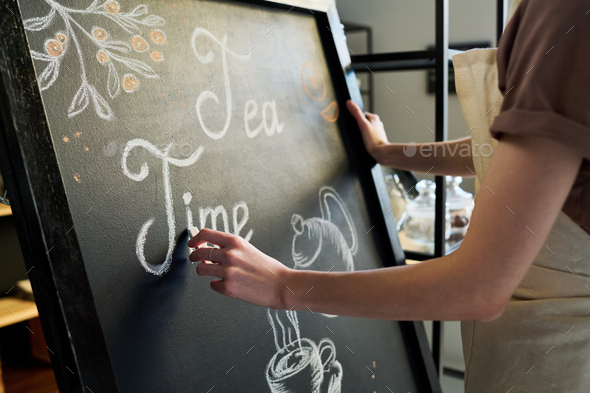 Close-up of young female worker of cafe drawing letters with chalk