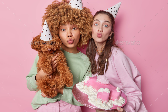 Horizontal shot of two women friends keep lips rounded send air kiss hold small poodle puppy and