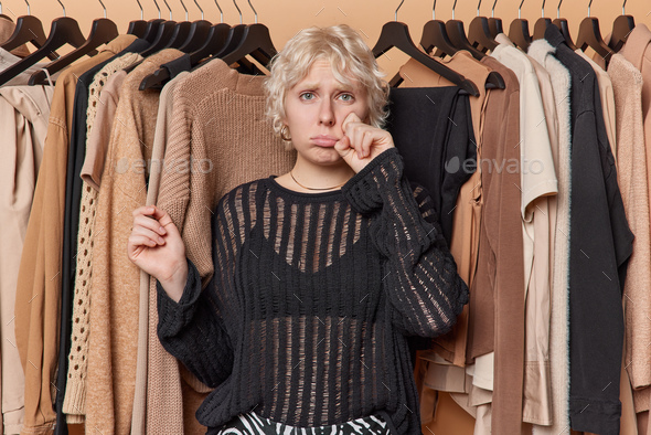 Stressed unhappy woman has nothing to wear cries and wipes tears wears  black jumper stands sad Stock Photo by wayhomestudioo