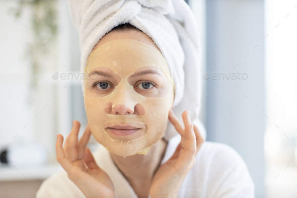 Lady in towel using cosmetic facial mask in home interior