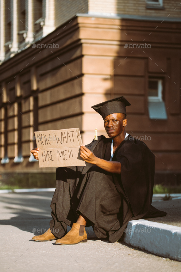 Happy black guy sitting with cardboard poster on street looking for job. University or college