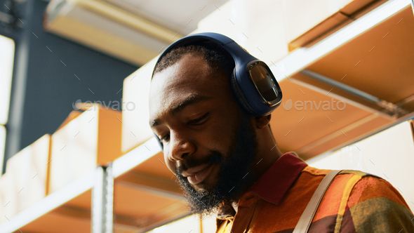 Male employee listening to music and working in depot - Stock Photo - Images