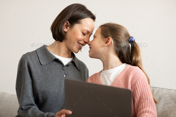 Happy european teen girl rubbing nose with millennial mom, have fun with laptop, surfing in internet