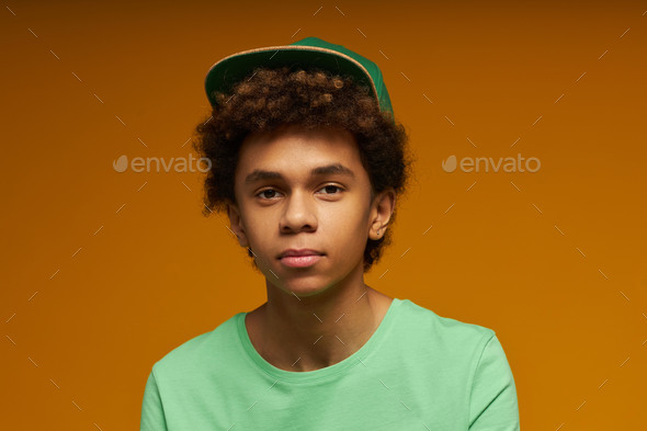 Cute teenage boy with neutral facial expression wearing green t-shirt and cap