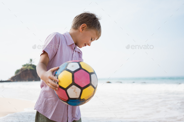 Little blond boy playing colorful ball at sea cost in summer day - Stock Photo - Images