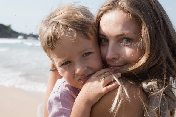 Beautiful young mother and son hugging at beach in sunny summer day - Stock Photo - Images