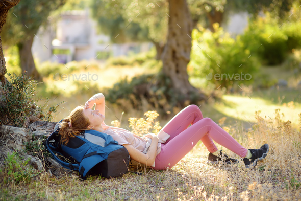 Young woman hiking in countryside. Girl is lying under the tree and having rest and relax.