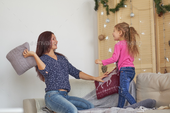 happy Mom and daughter having pillow fight at home. mother and little girl have fun together.