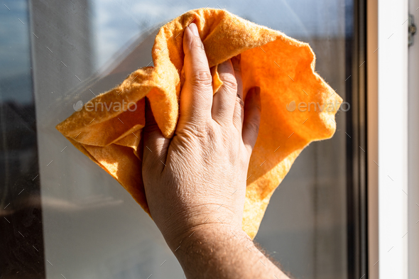 male hand wipes surface of window glass with rag