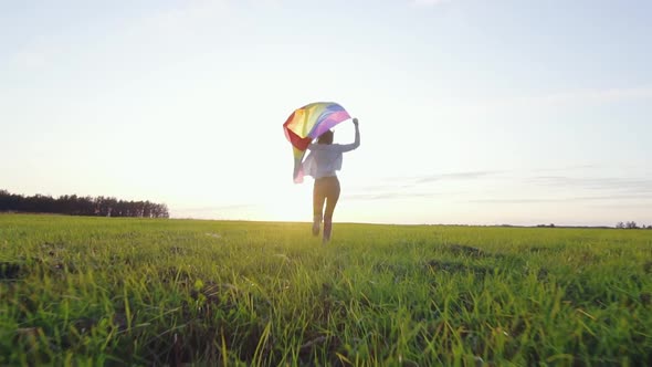 Young Positive Woman Runs Across Field with LGBT Flag Slow Mo Rear View alt