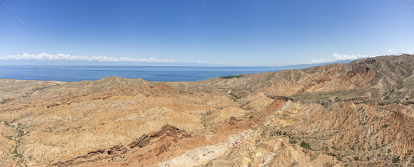 Wide panorama of the desert of Skazka Canyon with lake Issyk-Kul in the background. - Stock Photo - Images
