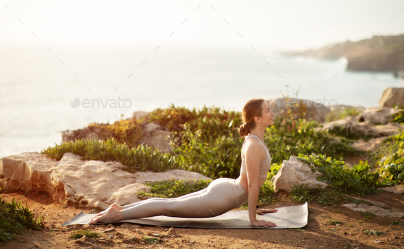 Glad young caucasian lady in sportswear practicing yoga on ocean beach,  enjoy rest, relax and free Stock Photo by Prostock-studio | T-Shirts