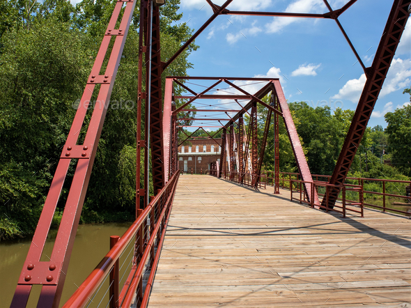 Iron bridge with a wooden floor over the river Stock Photo by wirestock