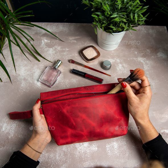 Top view of handmade leather red makeup bag on her hands with makeup kits on the table