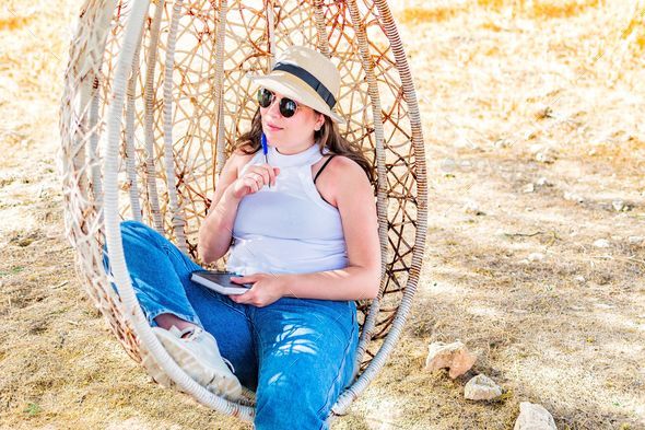 Middle Eastern Woman sitting in hanging rattan egg chair, relaxing summer