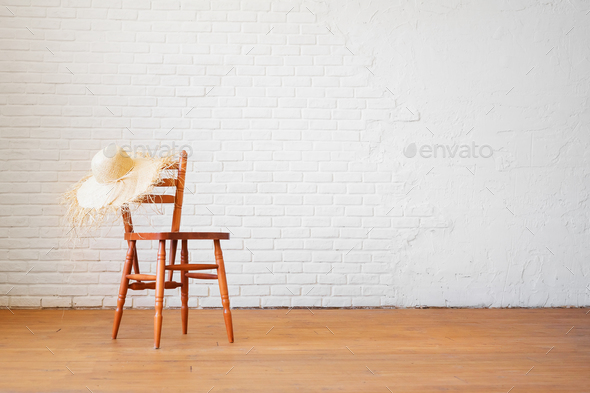Retro chair with a straw hat on the background of an empty brick white wall.