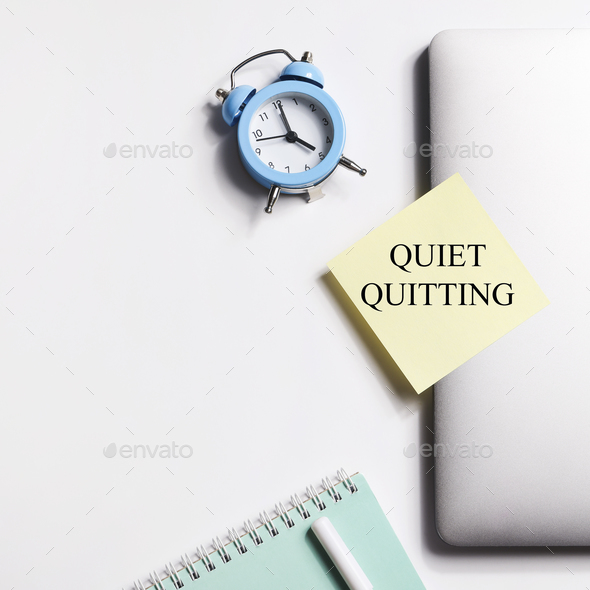 quote 'Quiet quitting' on yellow sticker on computer with clock and notebook. work life balance