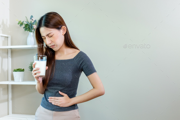 Asian female unhappy holding glass milk and stomach ache after drinking ...