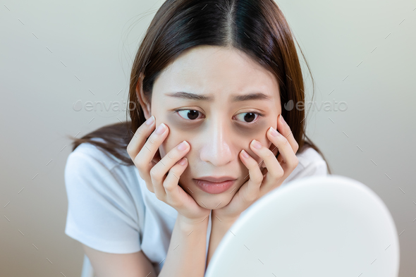 Asian young female stress looking mirror have dark eye circles from staying up sleepy late.