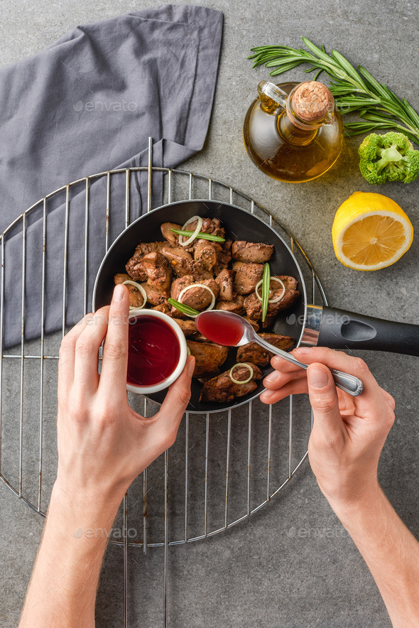 cropped view of woman adding souce in fried meat with oil, broccoli and lemon - Stock Photo - Images