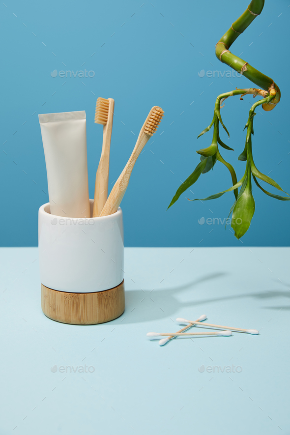 holder with bamboo toothbrushes, toothpaste in tube, ear sticks and bamboo stem on table and blue