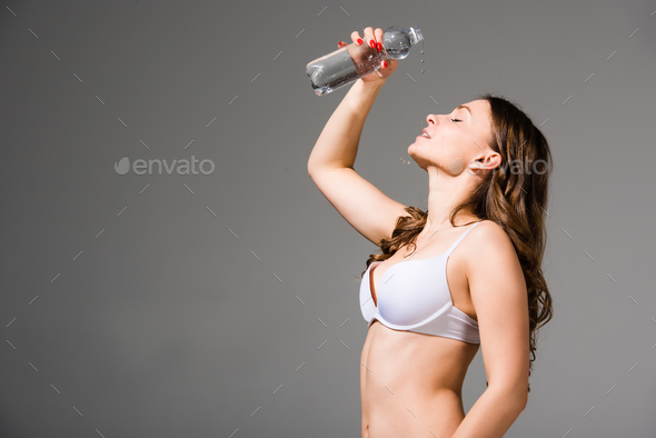 sexy woman in sport bra and panties holding sport bottle and looking at  camera isolated on grey Stock Photo by LightFieldStudios