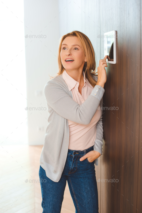 pretty blonde woman using smart home control panel and holding hand in pocket