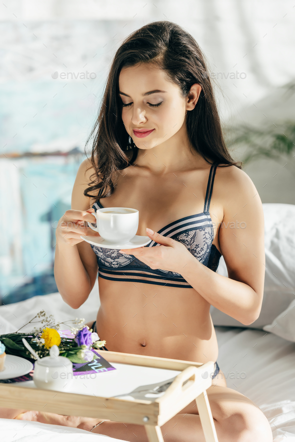 beautiful brunette woman in underwear holding cup while sitting