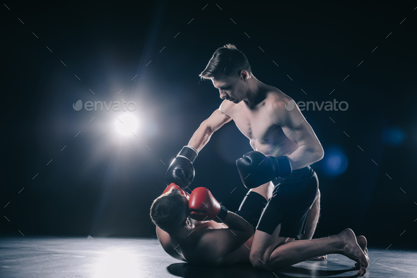 shirtless strong mma fighter in boxing gloves standing on knees above ...