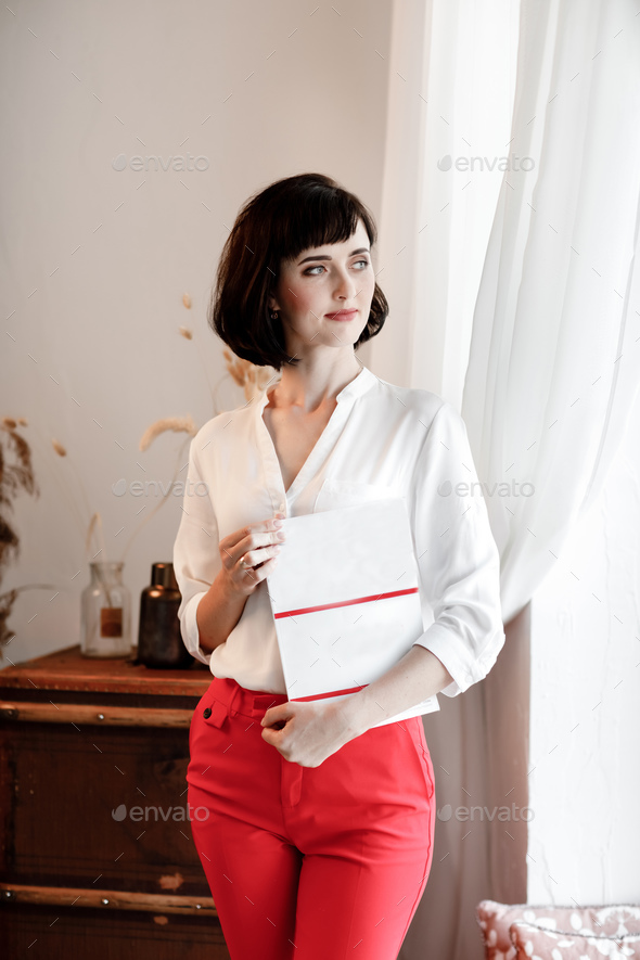 beautiful young woman with dark short hair holding a magazine with mock up. girl in a white shirt