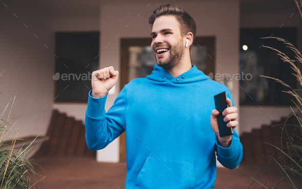 Cheerful male in electronic headphones enjoying music podcast dancing at city street