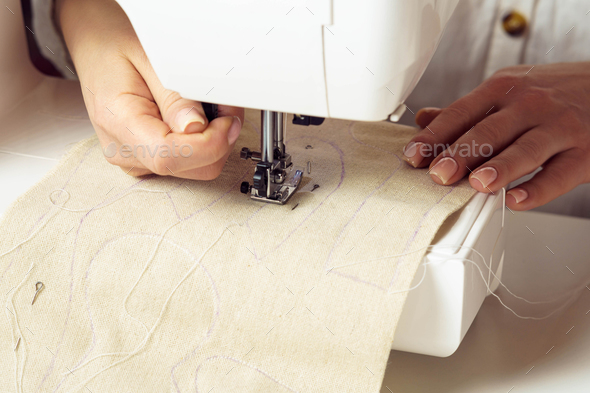 Dressmaker hand using sewing machine, putting white soft fabric with stitch contour on needle plate