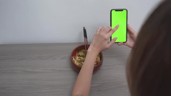 A Woman Using Smartphone With Green Touch Screen While Eating At Home alt
