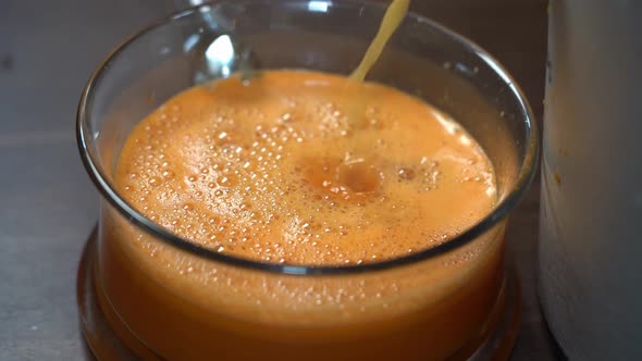 Fresh carrot and orange juice poring down into glass bowl from juice machine - Slow motion alt