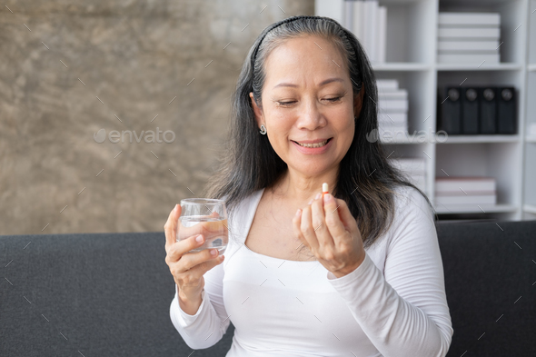 Happy elderly woman taking a pill according to the doctor order while sitting on the sofa.